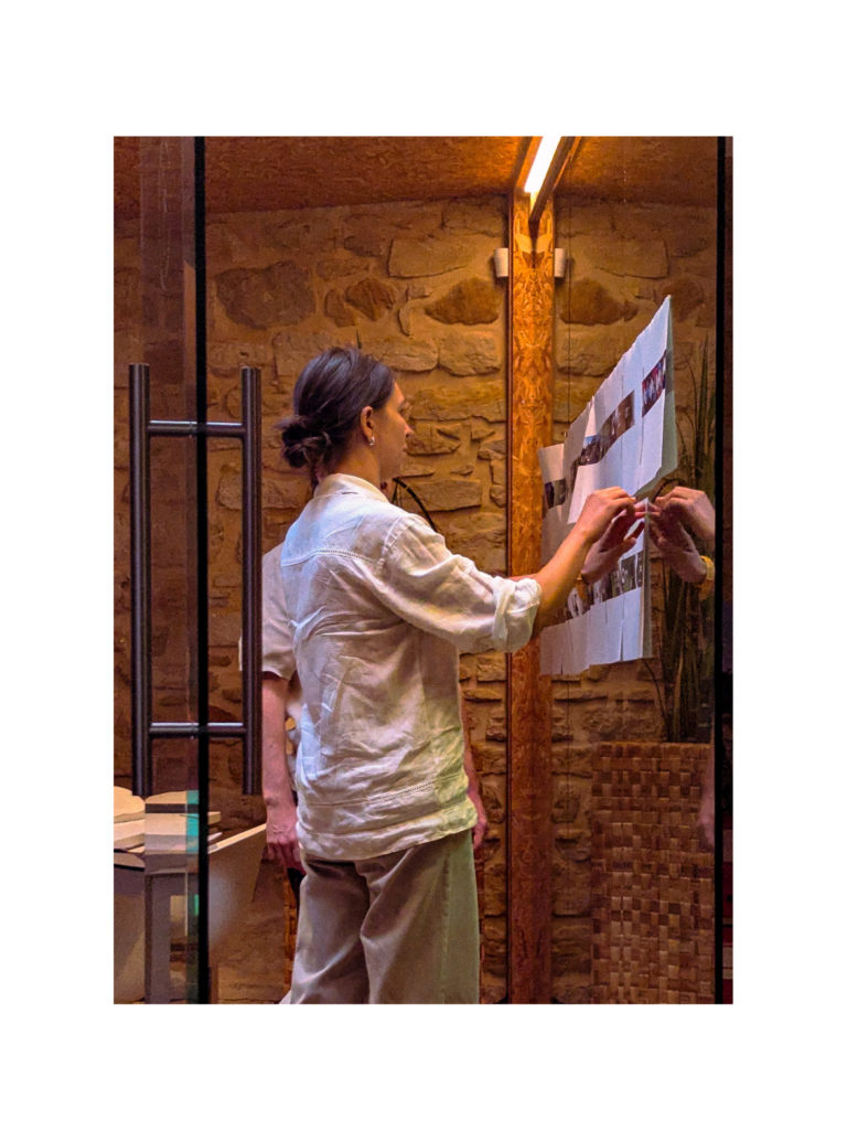 Femme de dos accrochant une série de petites photos sur une paroi en verre.