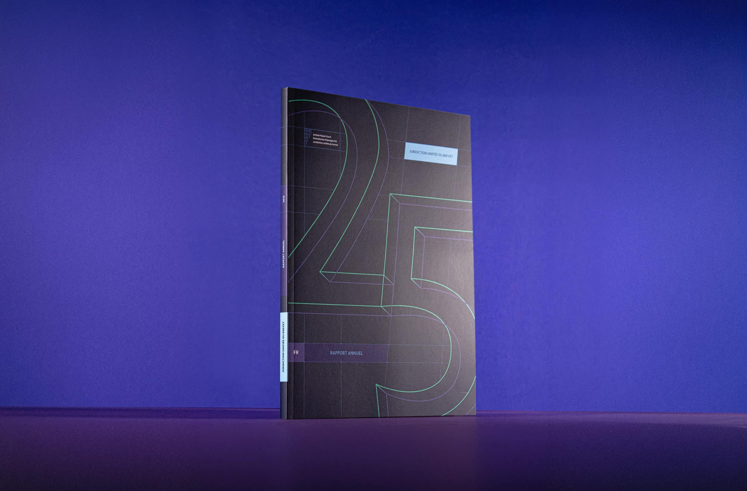 Brochure du rapport annuel de la Juridiction unifiée du brevet posée sur un fond violet, présentant une couverture texturée avec des lignes vertes fluo.