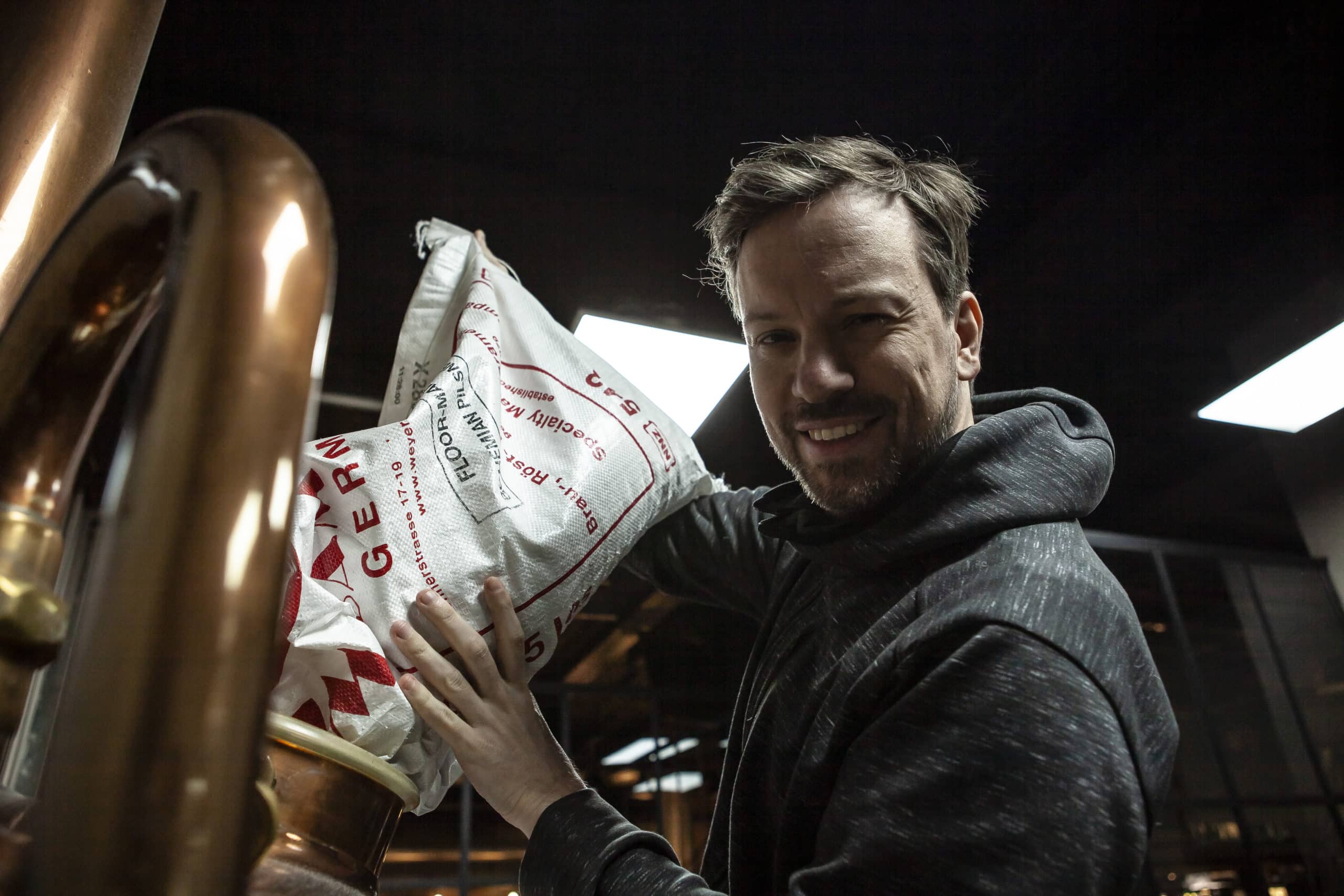 Homme souriant versant un grand sac de grain dans une cuve en cuivre.