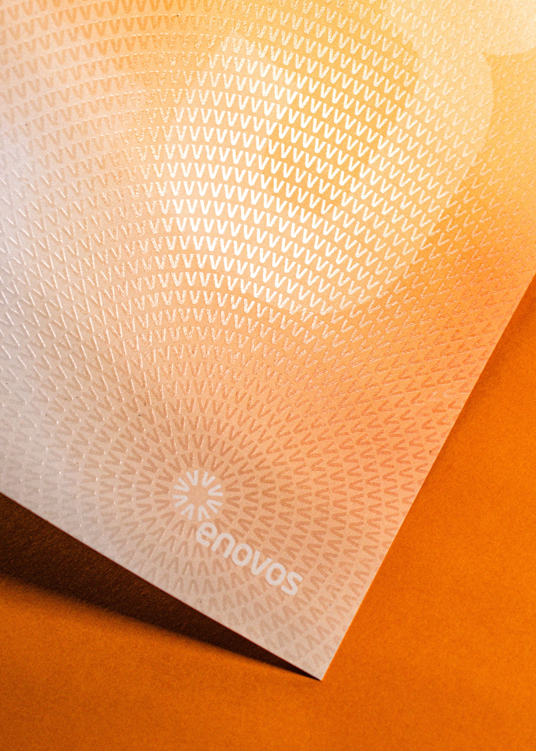 Plan rapproché de la texture tactile d'un document Enovos avec son nouveau logo hélice et texte en majuscules.