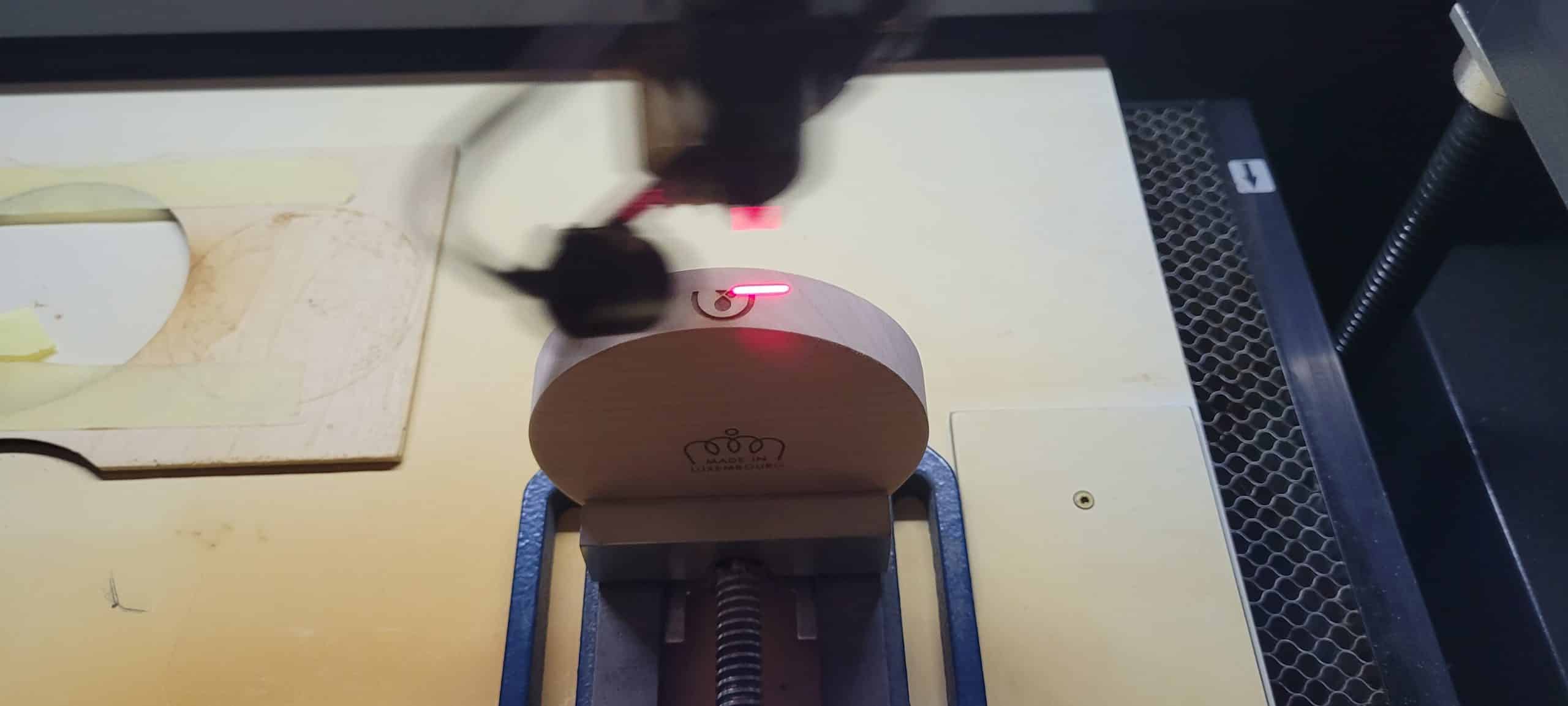 Vue de dessus d'un rayon laser rouge gravant un logo sur une pièce de bois ronde dans une machine de gravure.