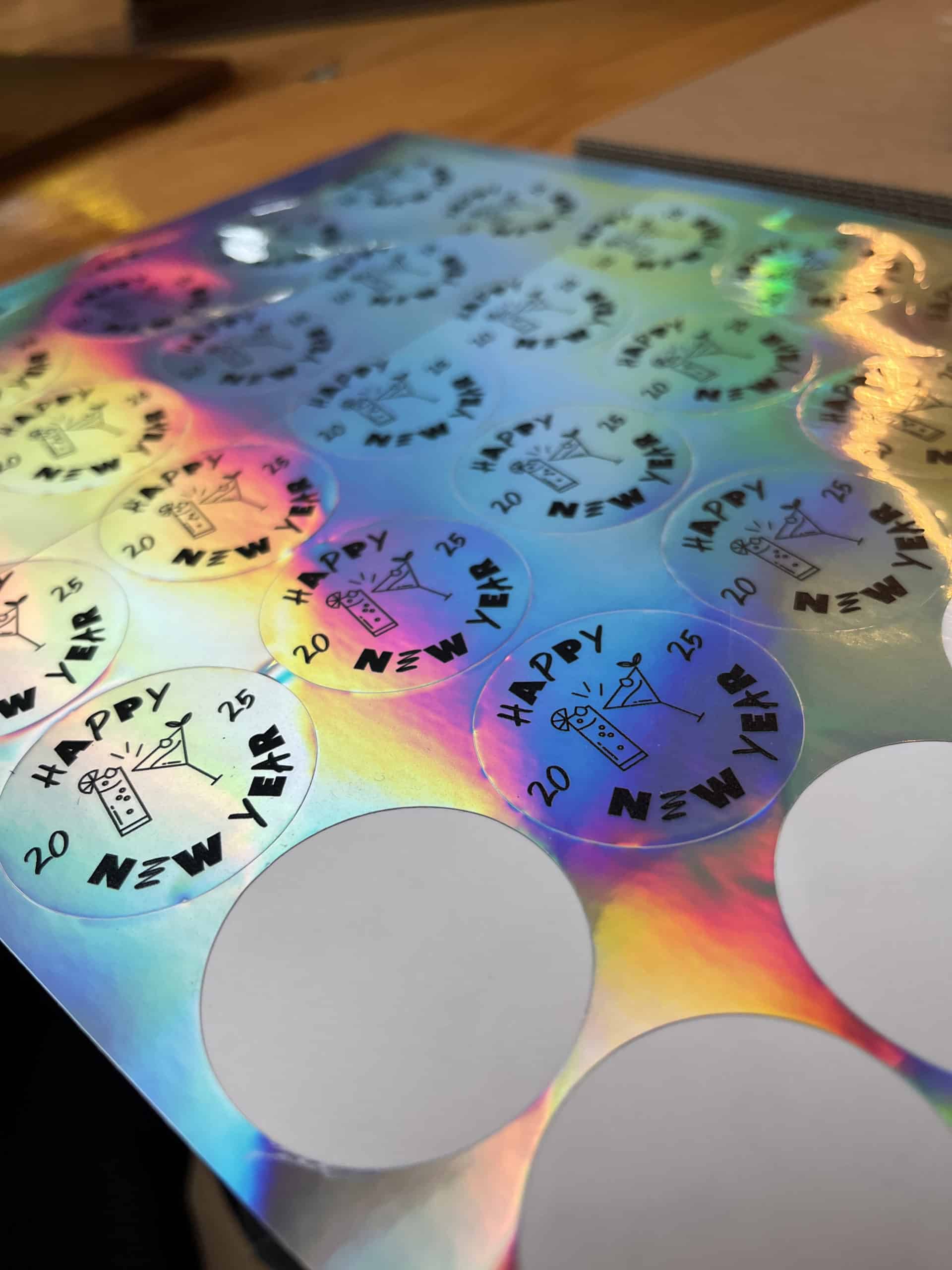 Planche d'autocollants ronds et holographiques imprimés avec des verres à cocktail et le texte Happy New Year 2025.