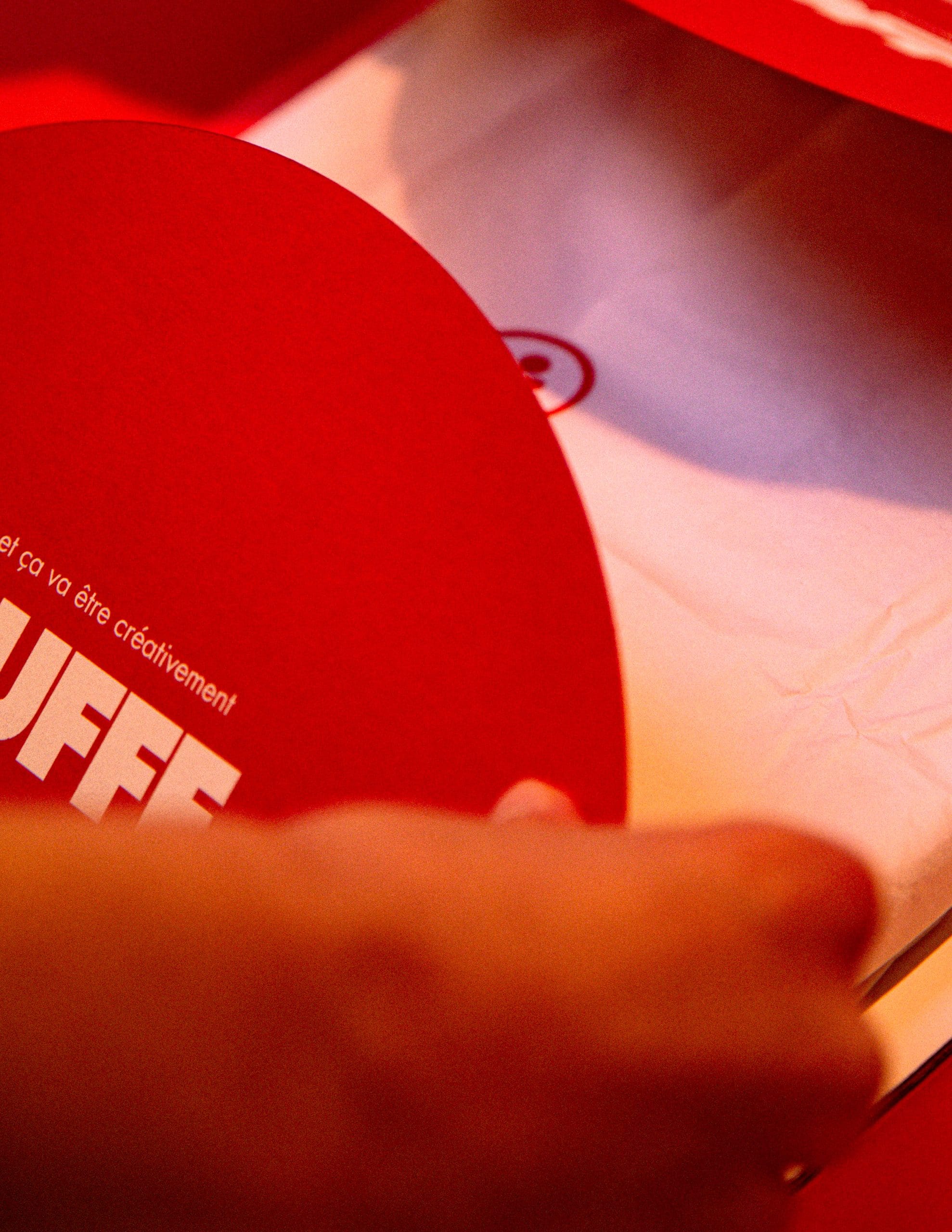 Mains ouvrant un colis rouge contenant un t-shirt blanc et une carte de remerciement.