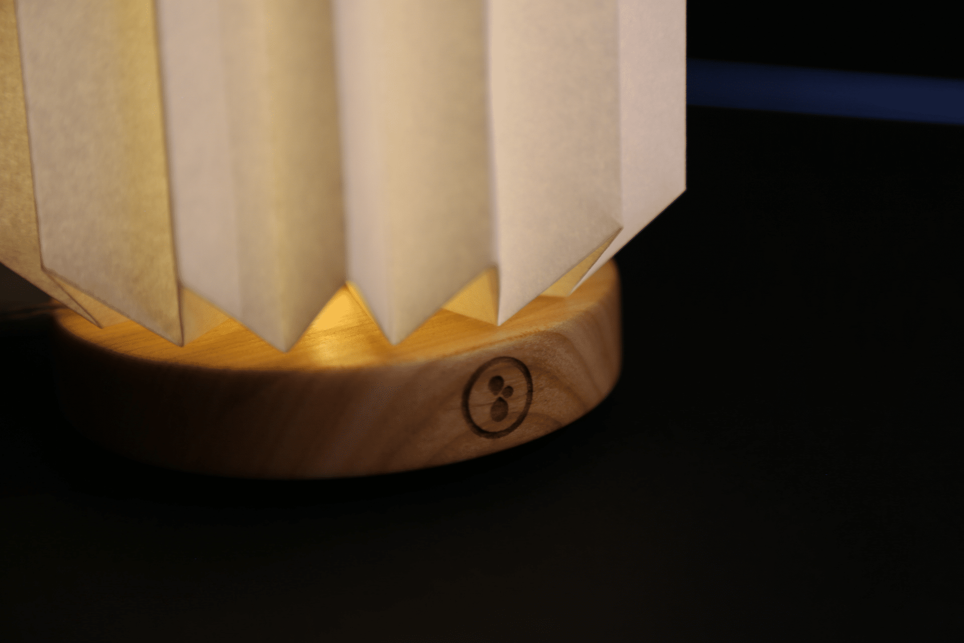 Gros plan de la base en bois gravée d'un logo circulaire d'une lampe plissée allumée.