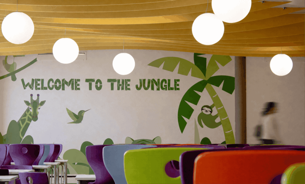 Fresque murale avec l'inscription 'WELCOME TO THE JUNGLE', suspensions lumineuses sphériques blanches et chaises d'école multicolores